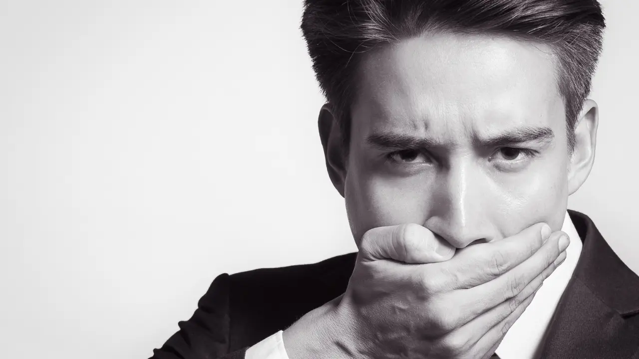口を手で押さえるスーツの男性
